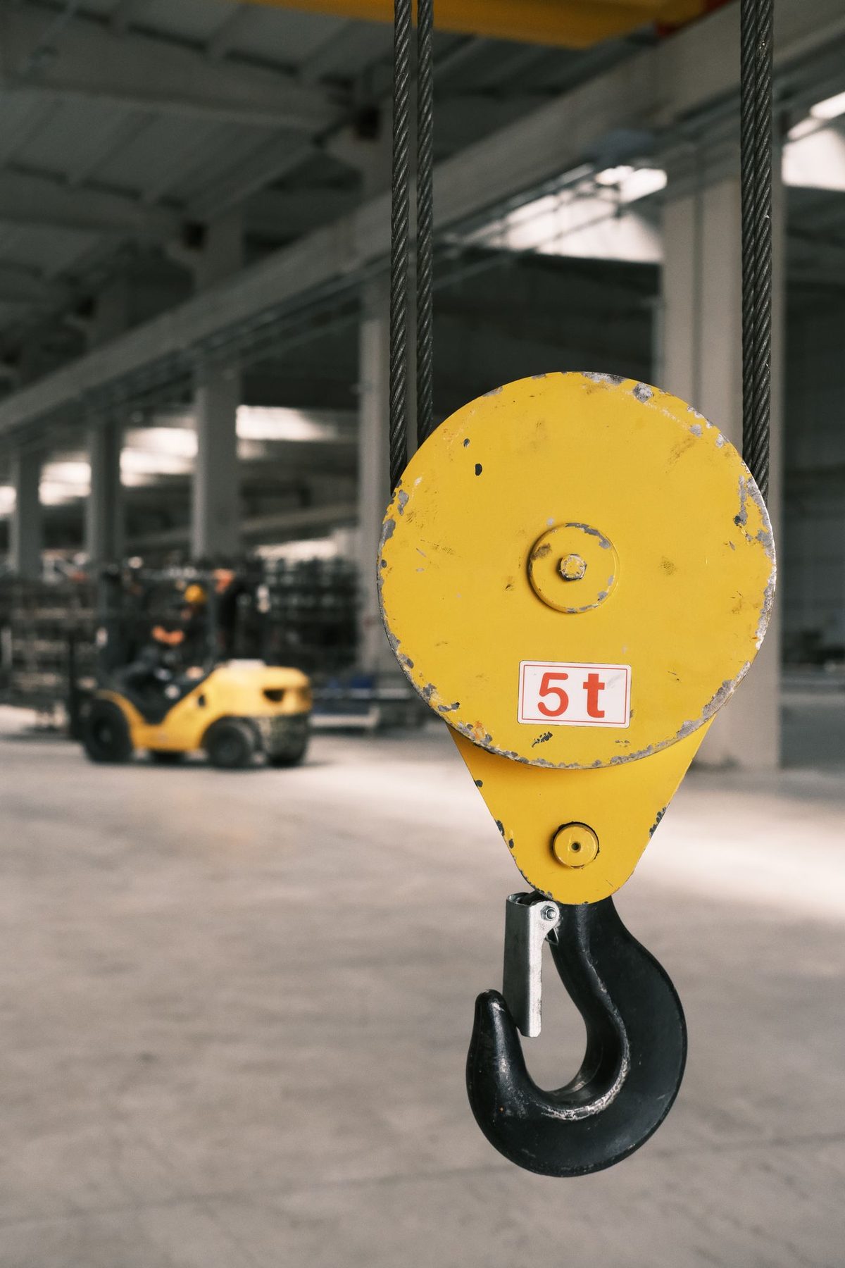 A crane block and hook rated 5 t, hanging on wire rope in a factory bay